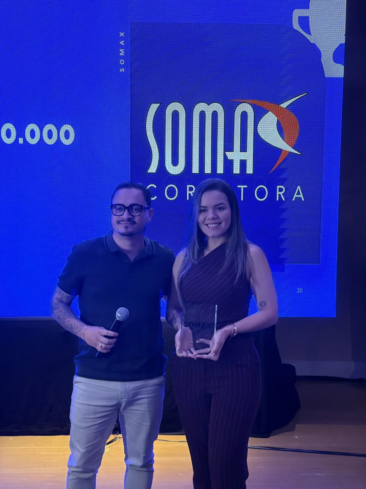 Sócios da Somax no palco da premiação da NN Gestão & Escala, segurando o troféu, com o logo da Somax projetado no telão.